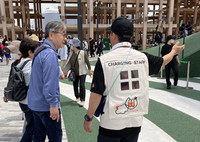 A pavilion guide at the Osaka Expo (right) tests smart wear developed by auto parts maker Toyoda Gosei, which is equipped with perovskite solar cells. (Courtesy of the company)