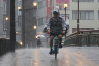 People travel by bicycle and on foot in heavy rain in the city of Kumamoto on Monday.